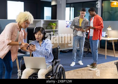 Une équipe diversifiée collabore pour une startup ; une femme en fauteuil roulant travaille sur un ordinateur portable Banque D'Images
