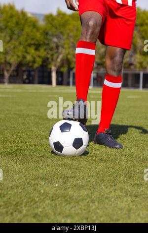 Joueur de football afro-américain se tient sur le terrain de football avec le pied sur la balle Banque D'Images
