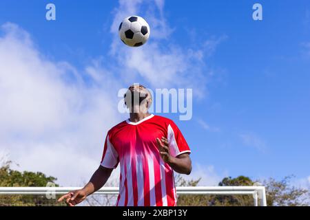 Joueur de football afro-américain dans un maillot rouge et blanc équilibrant le ballon de football sur la tête Banque D'Images