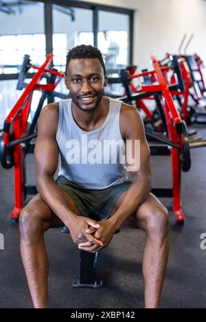 Homme afro-américain fort est assis sur le banc de gymnastique, souriant avec confiance après l'entraînement Banque D'Images