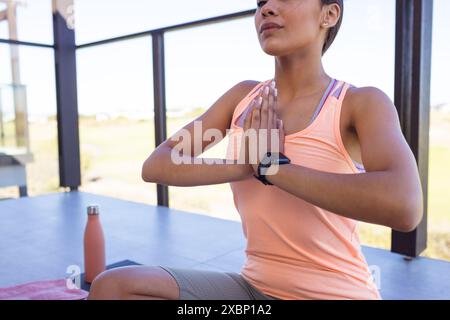 Femme biraciale heureuse pratiquant le yoga, portant une tenue de fitness et smartwatch Banque D'Images