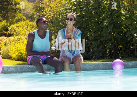 Couple diversifié se relaxant au bord de la piscine, profitant de boissons et du soleil d'été, se sentant heureux Banque D'Images