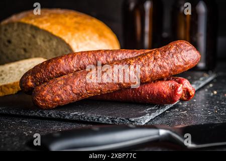 Saucisses de salami fumées sur une planche à découper sur une table noire. Banque D'Images