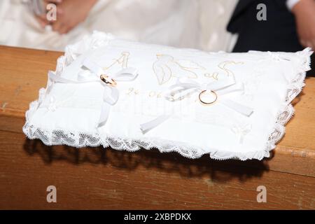 Élégant oreiller de mariage blanc avec broderie colombe, personnalisé avec les initiales et la date du couple, reposant sur un banc en bois rustique Banque D'Images