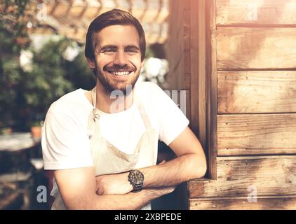 Sourire, portrait et homme serveur en plein air avec les bras croisés pour le positif, la confiance et la carrière. Heureux, fierté et barista masculin ou travailleur hôtelier avec Banque D'Images