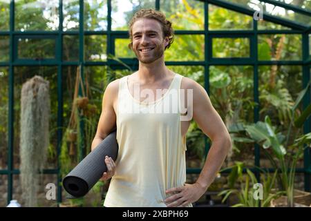 Praticien de yoga masculin caucasien tenant un tapis de yoga et souriant avec confiance Banque D'Images