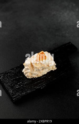 Rouleau de meringue. Protéines fouettées et sucre, garniture - fromage à la crème à base de fromage à pâte molle et de crème sur une planche à découper noire Banque D'Images