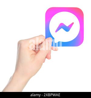 La main tient en papier l'icône de l'application mobile Facebook Messenger, sur un fond transparent. Facebook Messenger est une application de messagerie instantanée propriétaire américaine Banque D'Images