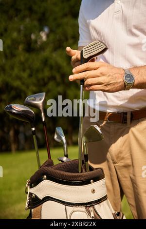 Un jeune homme élégant portant des vêtements élégants, mettant ses clubs de golf dans un sac sur un terrain vert dans un club de golf prestigieux. Banque D'Images