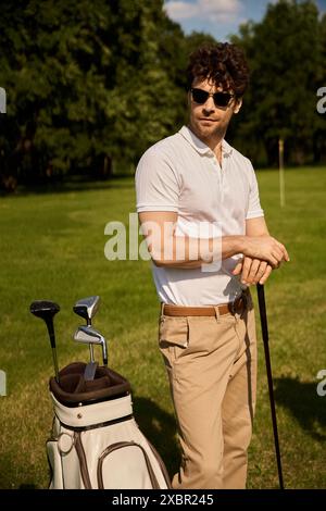 Un homme se tient élégamment à côté de son sac de golf sur un terrain vert au club de golf, incarnant un style de vie ancien argent. Banque D'Images