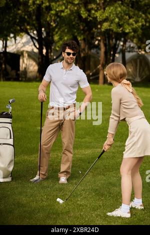 Un jeune homme et une jeune femme jouent élégamment au golf dans un parc, incarnant luxe et sophistication dans leur tenue et leurs balançoires. Banque D'Images
