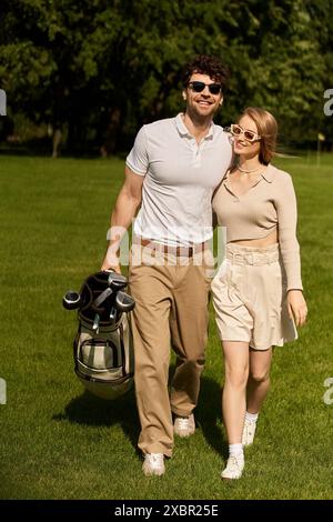 Un jeune couple dans une tenue élégante marchant tranquillement sur un parcours de golf luxueux par une journée ensoleillée. Banque D'Images