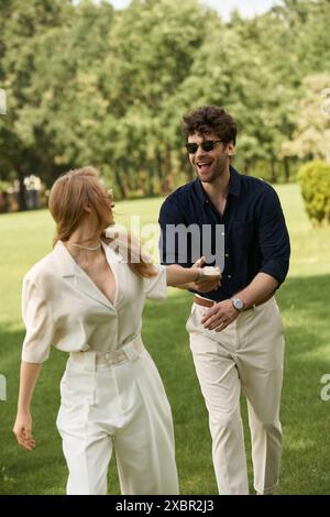 Un beau jeune couple dans des vêtements élégants profitant d'une promenade tranquille à travers un parc verdoyant, incarnant un style de vie luxueux vieux-argent. Banque D'Images