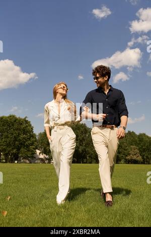 Un beau jeune couple en vêtements élégants se promène dans un champ vert, incarnant un style de vie luxueux. Banque D'Images