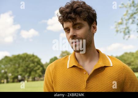 Un homme élégant dans une chemise jaune vif se tient au milieu de la verdure luxuriante d'un parc par une journée ensoleillée. Banque D'Images