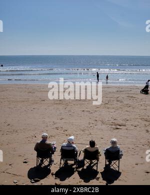 Quatre retraités se sont assis dans une rangée sur la plage au large du Cobble Landing à Filey, North Yorkshire East Coast, au nord de l'Angleterre, au Royaume-Uni Banque D'Images