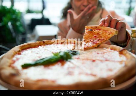 Gros plan d'une personne ramassant une tranche de pizza fraîchement préparée dans un restaurant. Concentrez-vous sur la pizza, créant un sentiment d'appétit et de plaisir Banque D'Images