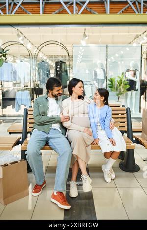 Une famille heureuse est assise sur un banc dans un centre commercial animé, profitant d'un moment de détente ensemble lors de leur sortie de week-end. Banque D'Images