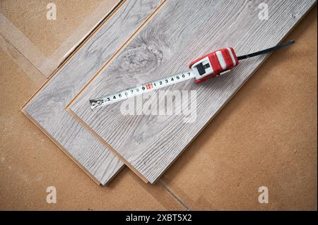 Vue de dessus du ruban à mesurer sur des planches de plancher en bois pour la rénovation de la maison et les travaux de construction. Ruban à mesurer métallique sur des échantillons de panneaux stratifiés avec motif et texture en bois pour les revêtements de sol. Banque D'Images