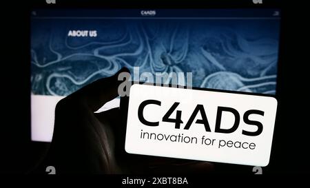 Personne tenant un smartphone avec le logo du Center for Advanced Defense Studies (C4ADS) devant le site Web. Concentrez-vous sur l'affichage du téléphone. Banque D'Images