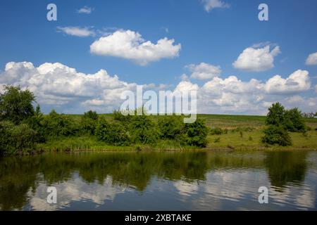 Paysage sereinement magnifique avec un lac reflétant le ciel bleu clair et les nuages blancs moelleux par une journée lumineuse et ensoleillée Banque D'Images