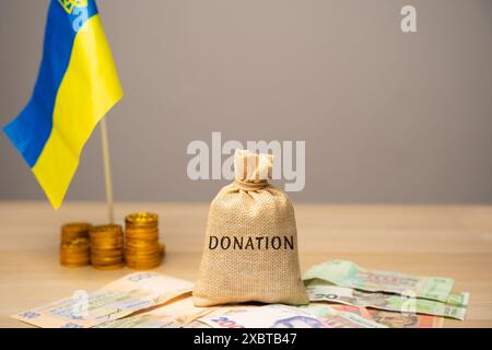 Don de sac d'argent, drapeau ukrainien et billets de hryvnia. Le concept d'aide monétaire à l'économie ukrainienne en raison de la guerre. Aide financière au Royaume-Uni Banque D'Images