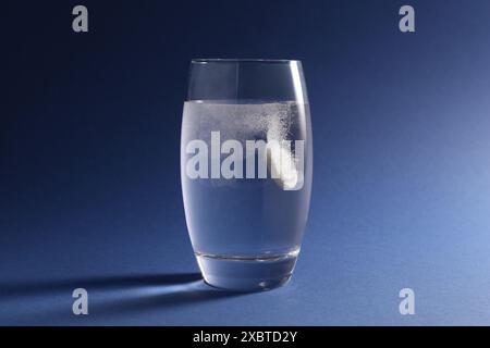 Pilule effervescente se dissolvant dans un verre d'eau sur fond bleu Banque D'Images
