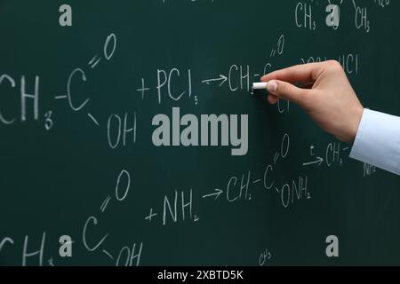 Professeur écrivant des formules chimiques avec de la craie sur un tableau vert, gros plan Banque D'Images