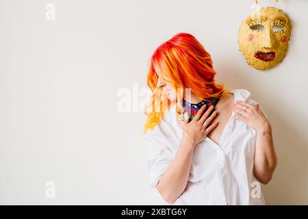 Une femme aux cheveux orange porte un collier et se tient devant un masque jaune. Concept de créativité et d'individualité, comme la dynamique de la femme Banque D'Images