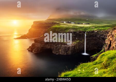 Cascade Mulafossur à l'heure du coucher du soleil. Ciel dramatique avec lumière dorée. Village de Gasadalur, île de Vagar, îles Féroé, Danemark. Photographie de paysage Banque D'Images
