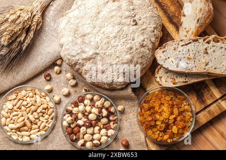 Pain avec ajout de noisettes, arachides et raisins secs dans une coupe et un pain entier. sur une planche de bois avec un bouquet de blé. Photo de haute qualité Banque D'Images