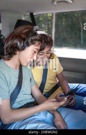 Des frères jumeaux avec des écouteurs regardent leurs téléphones portables assis dans la camionnette Banque D'Images