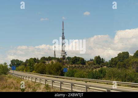 Une route goudronnée s'étend vers une colline en Espagne. Deux tours de communication se dressent sur la colline, visibles contre un ciel bleu avec des nuages blancs gonflés Banque D'Images