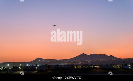 Un avion ATR monte dans le ciel crépusculaire au-dessus de Lanzarote, avec les lumières de la ville qui brillent en dessous et les montagnes silhouettes contre les nuances dégradées des soleils Banque D'Images