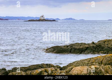 Le phare de Katland se trouve sur une petite île rocheuse, entourée par la mer, avec des collines lointaines en arrière-plan. Flekkefjord, Norvège Banque D'Images