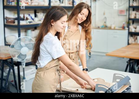 Femmes travaillant des potiers déployant des dalles d'argile ensemble dans un atelier de poterie Banque D'Images