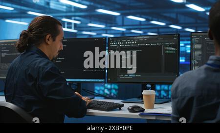 Les ingénieurs codent ensemble dans un hub de serveur de haute technologie, en utilisant des ordinateurs pour analyser les données, assurant un flux de données transparent. Collègues examinant l'infrastructure dans le centre de données, assurant l'intégrité et la sécurité du système Banque D'Images