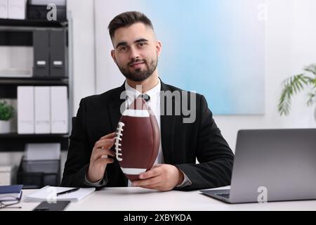 Jeune homme avec ballon de football américain à table dans le bureau Banque D'Images