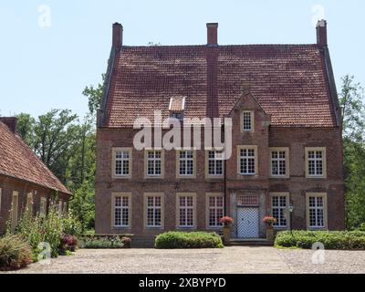 Grande maison en briques avec tuiles rouges et de nombreuses fenêtres, entourée d'arbres et d'un jardin bien entretenu par temps ensoleillé, ochtrup, muensterland, allemagne Banque D'Images