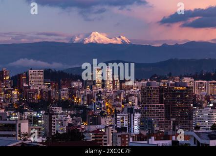 Edificios de Quito iluminados con el volcan Antisan al fondo al anochecer. Banque D'Images