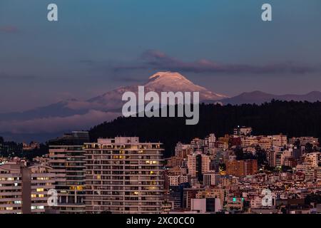 Edificios de Quito iluminados con el volcan Cayambe al fondo al anochecer. Banque D'Images