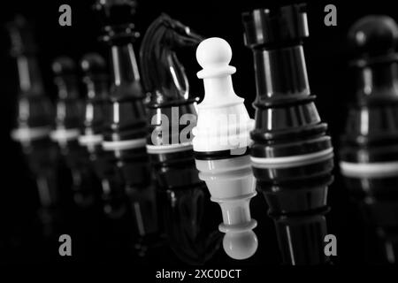 Gros plan du pion blanc parmi les pièces d'échecs noires avec réflexion Banque D'Images