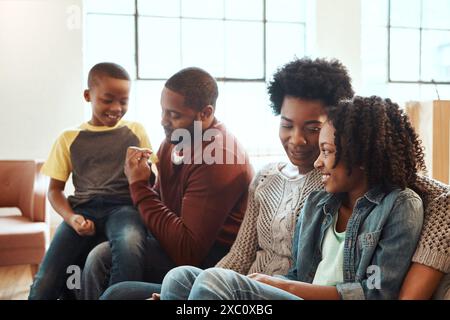 Heureux, se détendre et famille noire sur le canapé à la maison pour embrasser, amour et soins le jour des pères pour la célébration. Sourire, lier et enfants africains avec maman et Banque D'Images