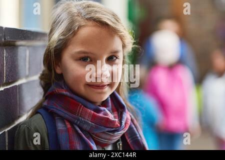 École primaire, couloir et portrait de fille par le mur pour l'érudition, l'apprentissage et la connaissance. Visage, heureux et étudiant avec le sourire dans le couloir pour Banque D'Images