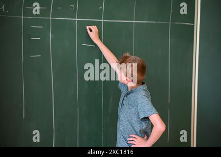 Le jeune étudiant écrit sur un grand tableau vert tout en résolvant un problème de mathématiques Banque D'Images