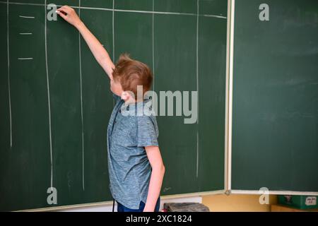 Le jeune étudiant écrit sur un grand tableau vert tout en résolvant un problème de mathématiques Banque D'Images