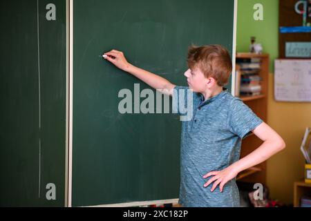 Le jeune étudiant écrit sur un grand tableau vert tout en résolvant un problème de mathématiques Banque D'Images