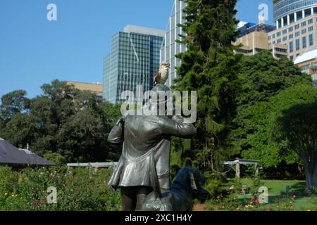 Royal Botanic Gardens Sydney, un Kookaburra repose sur la casquette de la statue Huntsman and Dogs dans le avec de grands arbres verts et la ligne d'horizon du CBD derrière Banque D'Images