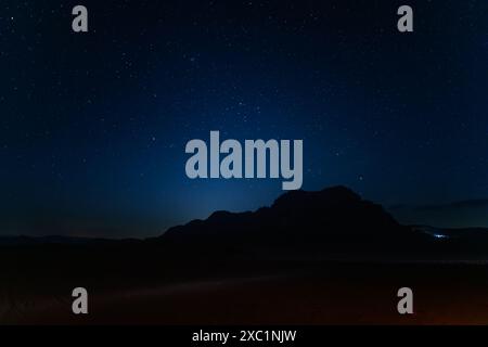 Un ciel nocturne captivant, parsemé d'étoiles, se couche sur la silhouette de la formation rocheuse Jabal al Qattar dans le paisible désert de Wadi Rum en Jordanie Banque D'Images