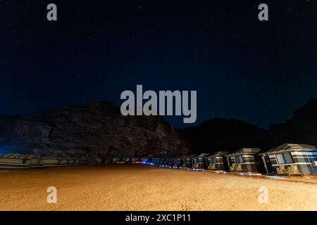 Ciel nocturne tranquille rempli d'étoiles au-dessus de la formation rocheuse unique Jabal al qattar à Wadi Rum, en jordanie, encadrée par un camp traditionnel du désert Banque D'Images